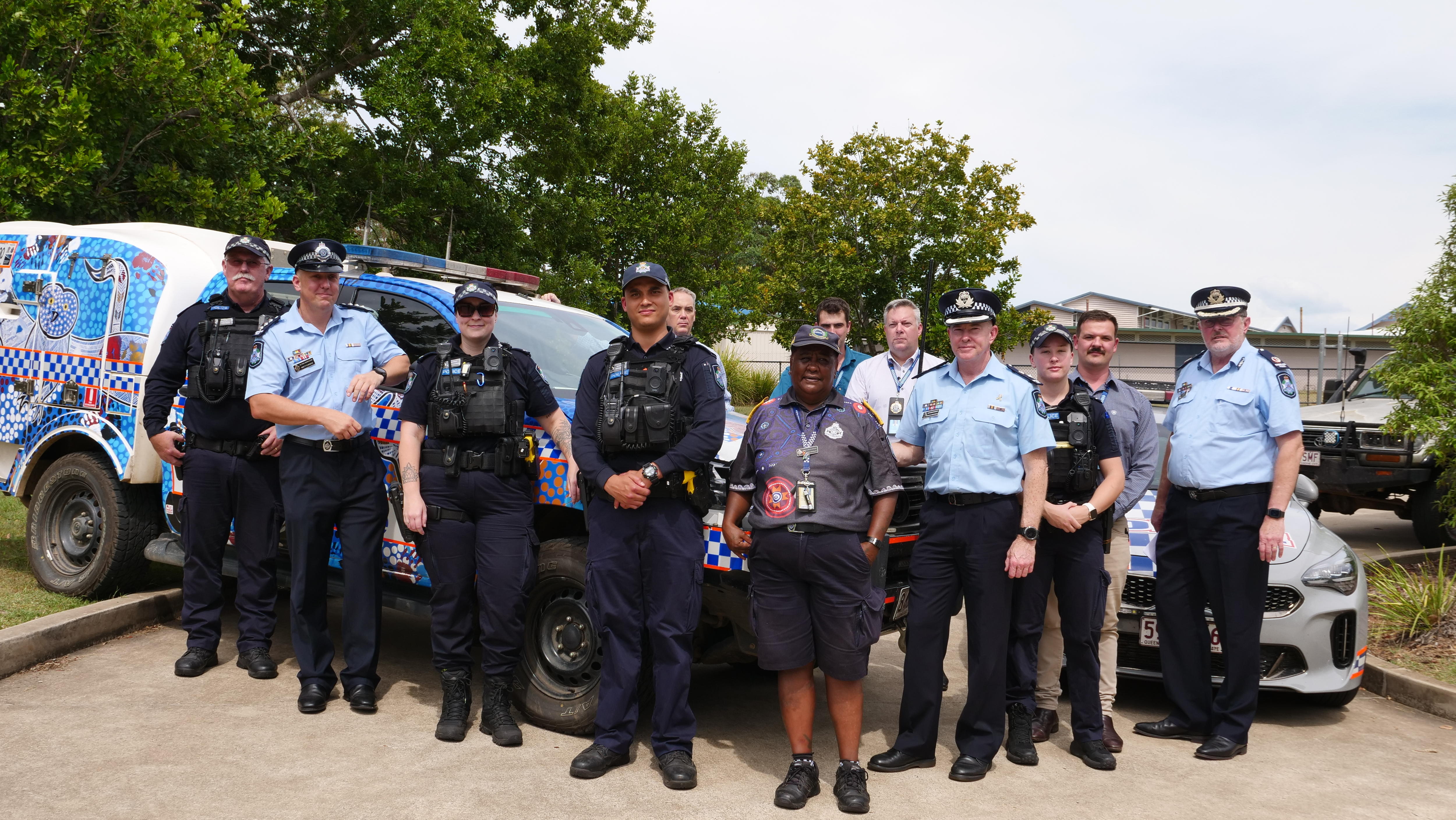 Grupo de policiais em frente a carros de polícia.