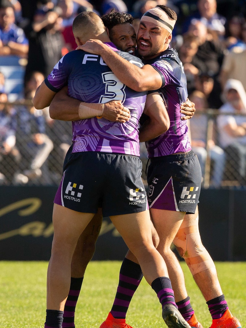 Josh Addo-Carr is hugged by two Storm teammates after scoring a try.