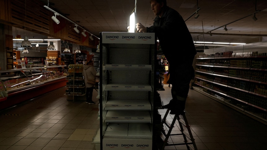 A supermarket worker installs a light powered by generator as Ukraine suffers electricity outages.