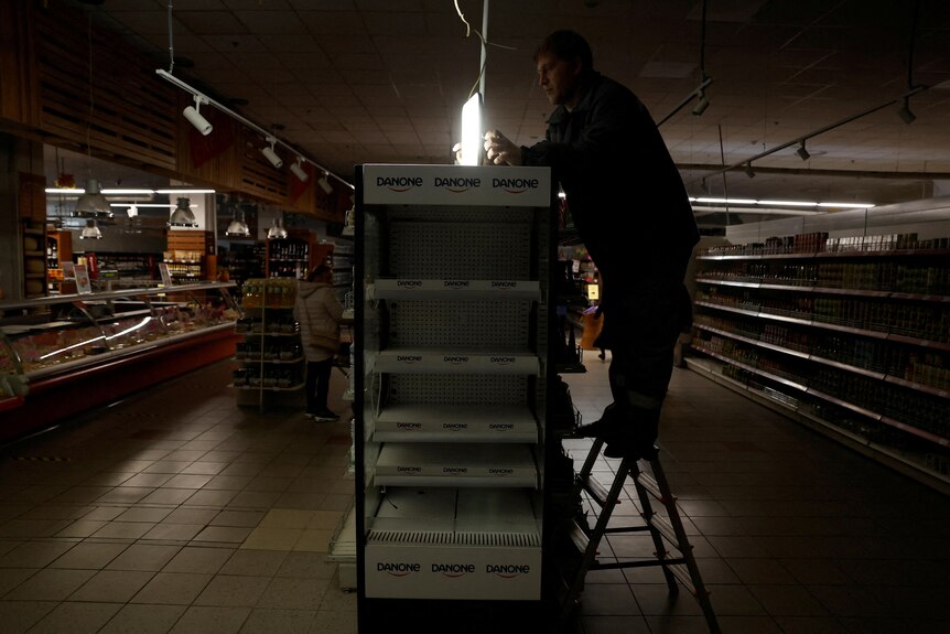A supermarket worker installs a light powered by generator as Ukraine suffers electricity outages.