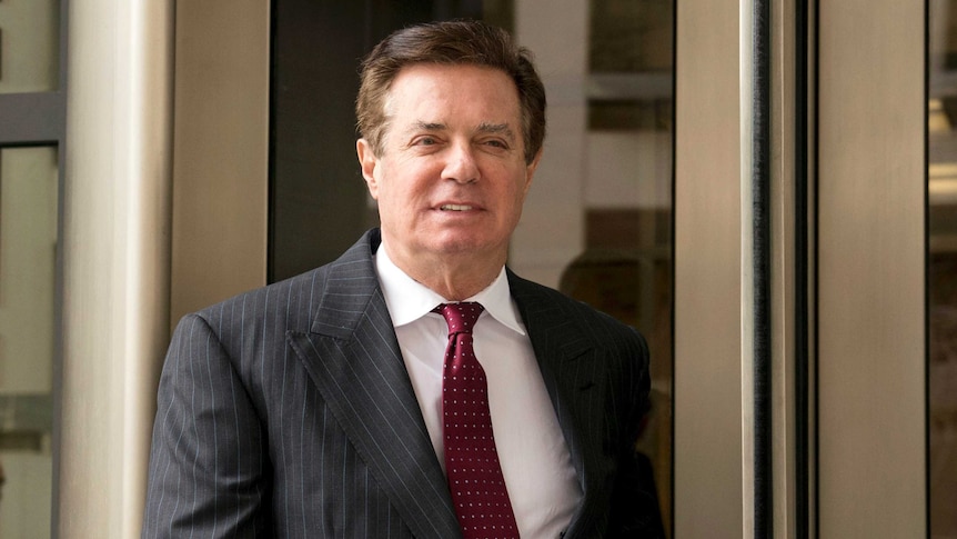 Paul Manafort walking wearing a dark pin striped shirt and red tie.