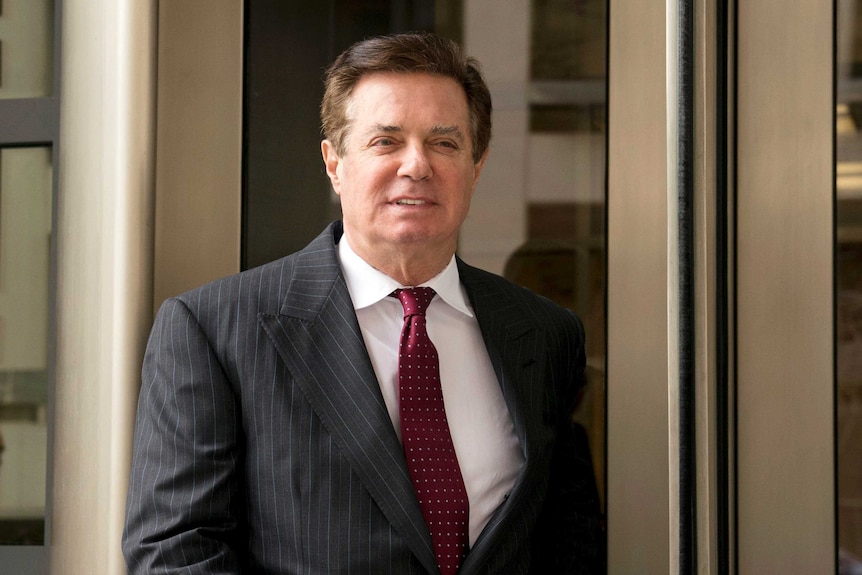 Paul Manafort walking wearing a dark pin striped shirt and red tie.