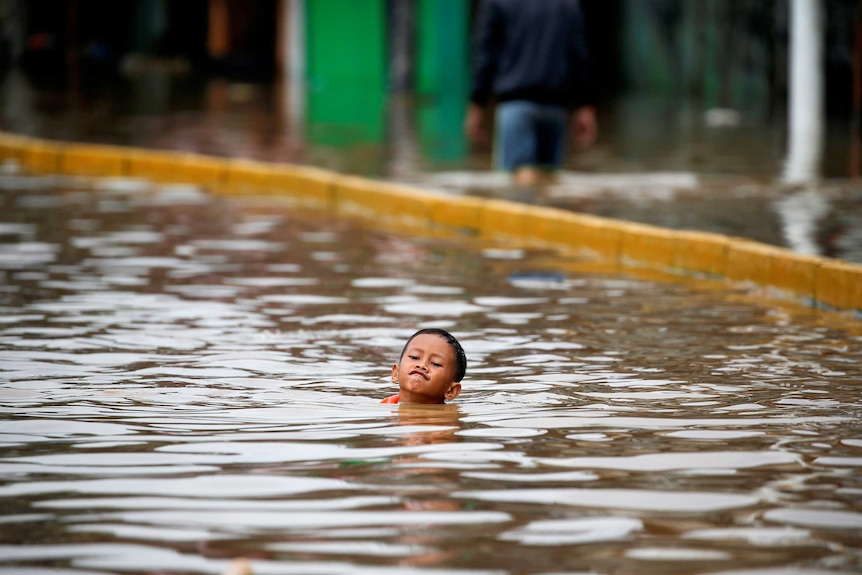 A small Indonesian child's face and head can be seen floating just above the water on a street in Jakarta.