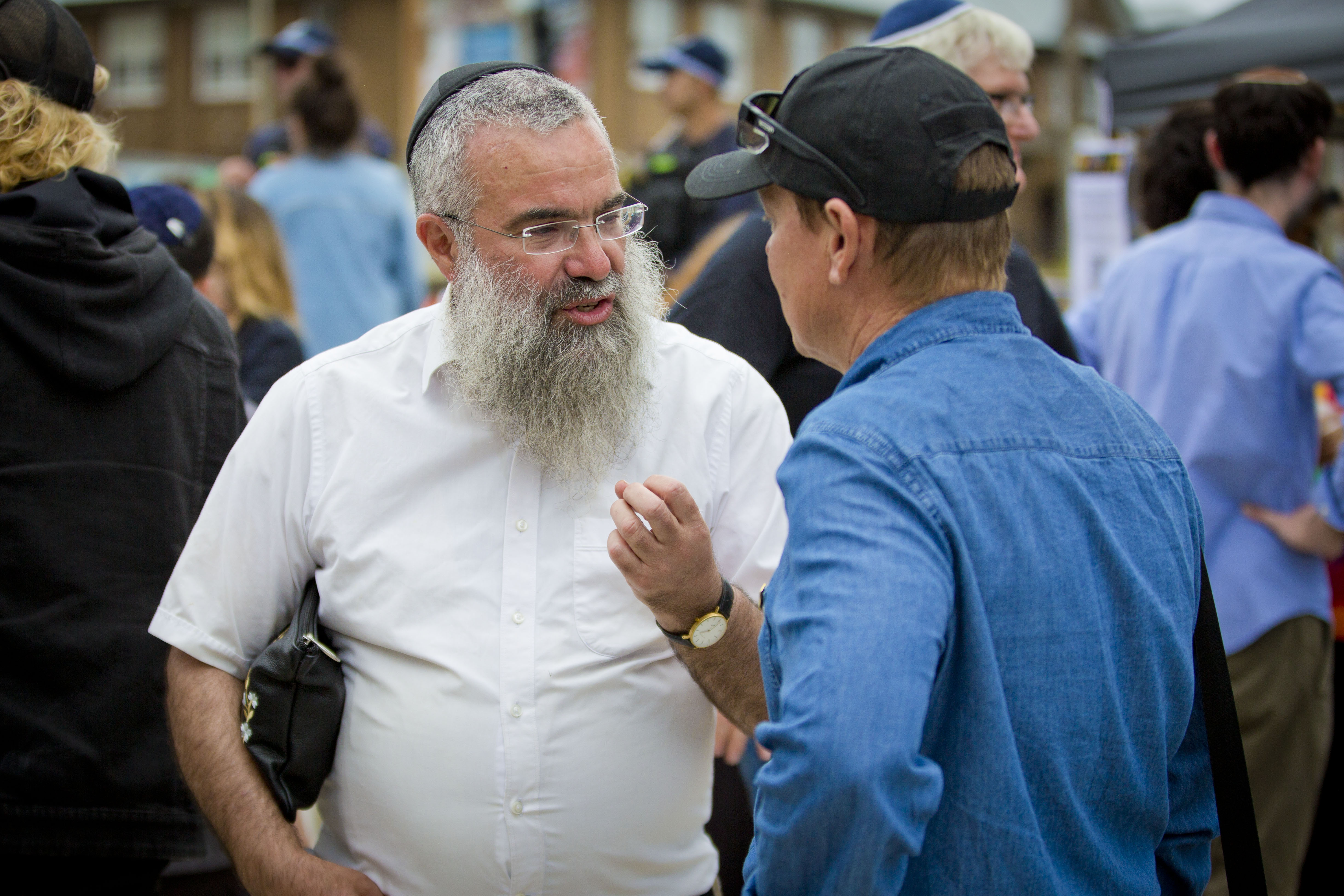 Um rabino de camisa e óculos fala com um membro do público em um memorial