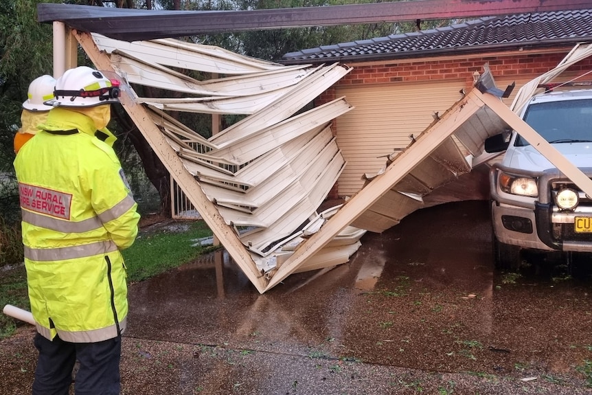 two emergency personnel inspect a collapsed carport with a ute unscathed