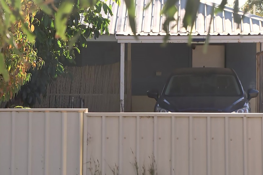 A car under a carport behind a fence, outside a house in Carnarvon.