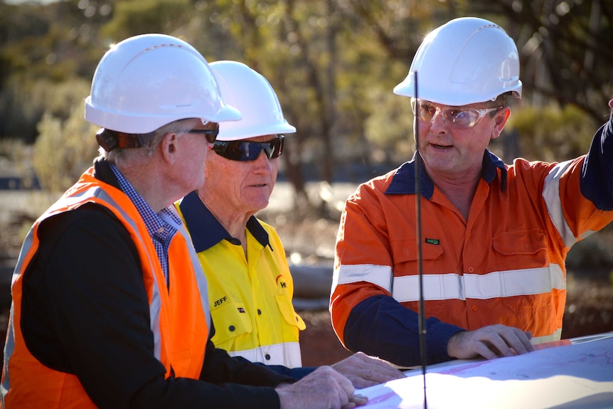 Three men wearing high-vis clothing on a mine site.