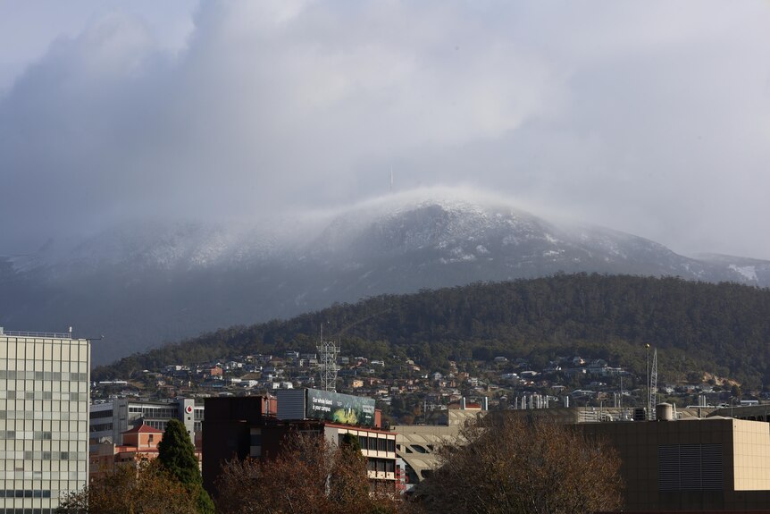 Kunanyi/Mt Wellington is blanketed by snow, with ominous grey clouds looming behind.