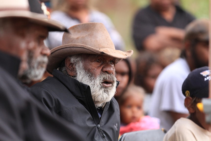 Indigenous man with tears on his face. He's wearing a black jacket and hat.