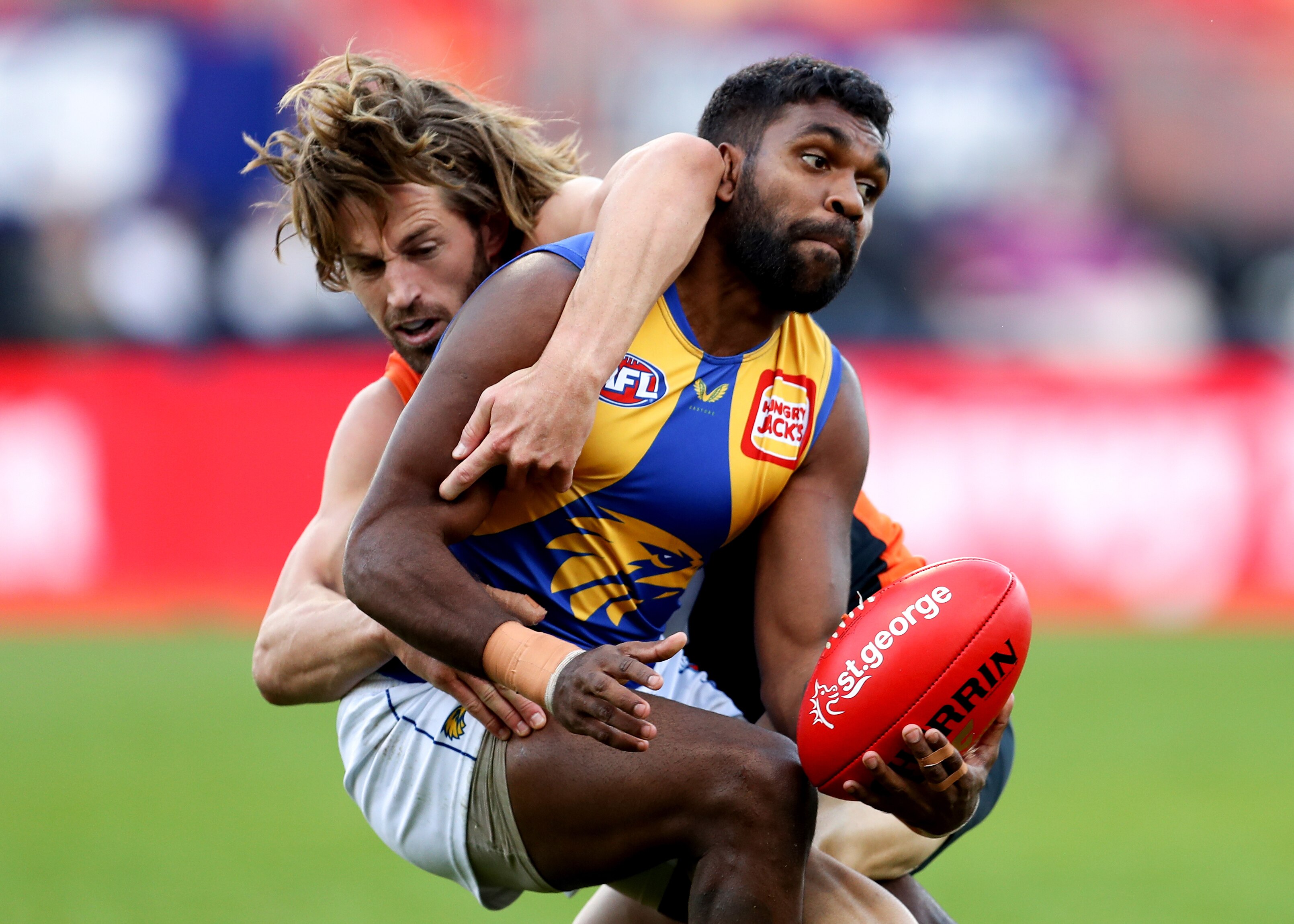 A West Coast Eagles AFL player attempts to pass the ball while being tackled by a GWS opponent.