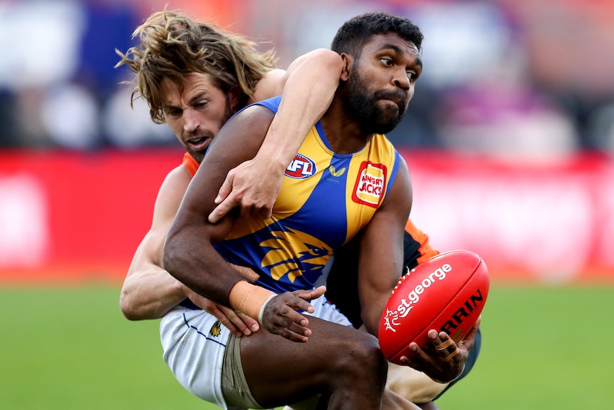 A West Coast Eagles AFL player attempts to pass the ball while being tackled by a GWS opponent.