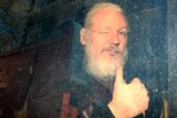WikiLeaks founder Julian Assange is seen through a dirty police van window as he winks and throws a thumb in the air.