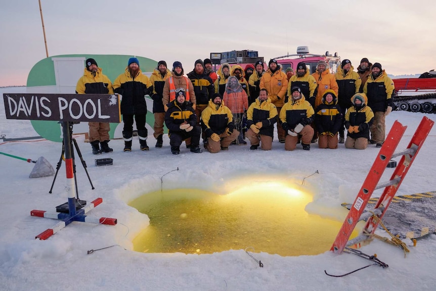 A group of Antarctic expeditioners stand around an icy pool at Davis station