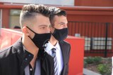 Two men wearing face masks walk along a city street.