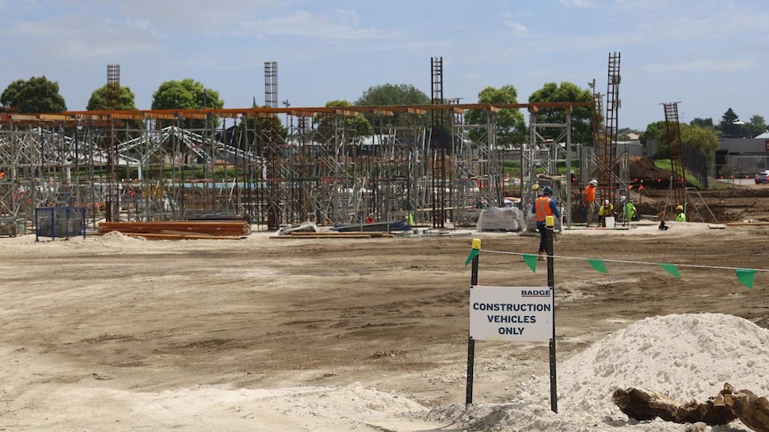 A sign reading "construction vehicles only" stands in front of the structural skeleton of a building and workers in high vis