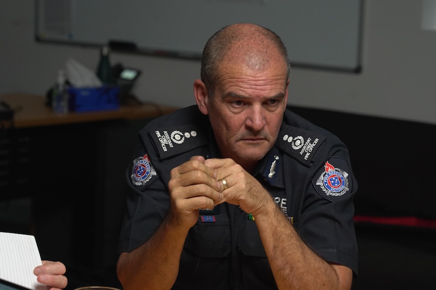 Mick Tisbury in a navy firefighter uniform listens in a meeting at a round table