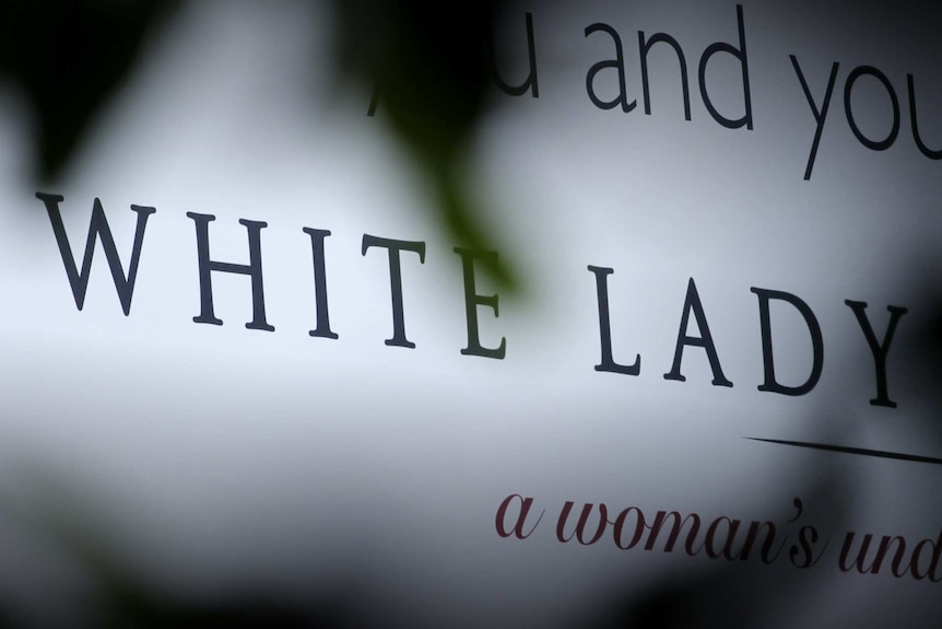 A close up of a White Lady Funerals sign, shot through some leaves