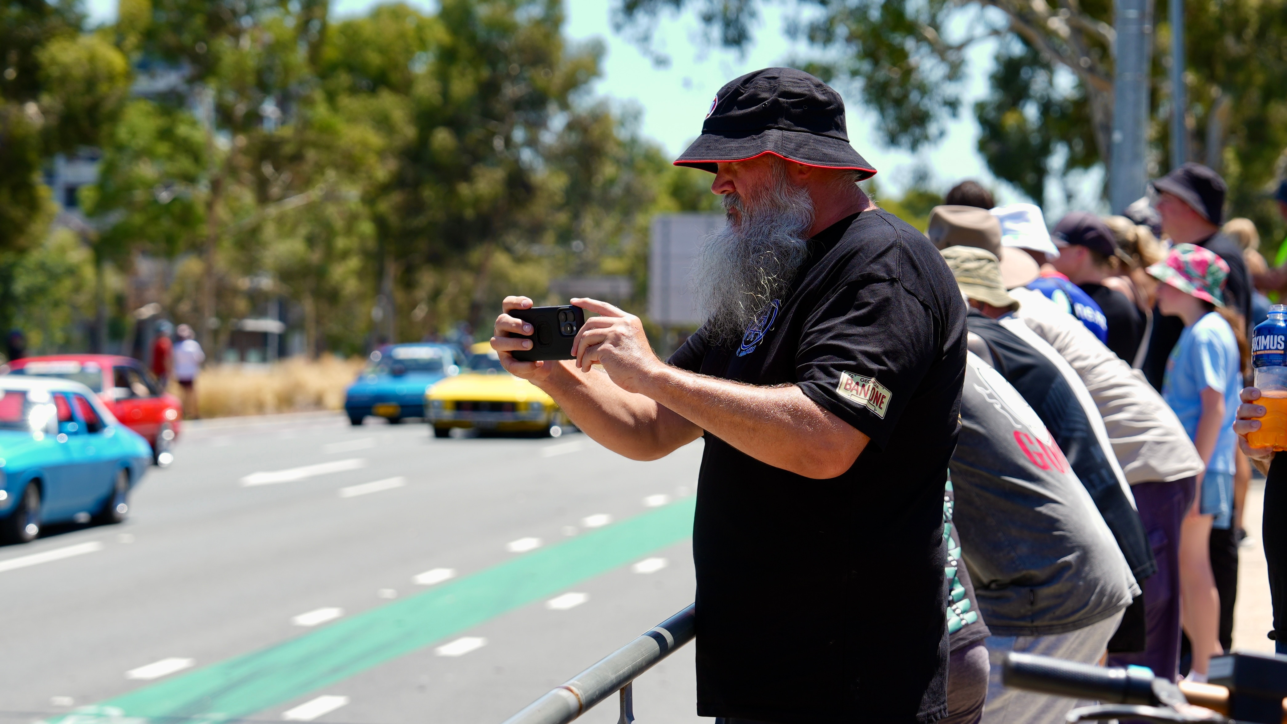 Um homem tira uma foto com seu telefone de um desfile de carros