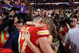 A male NFL player engages hugs girlfriend inside a stadium, with cheering fans, cameras and confetti surrounding them