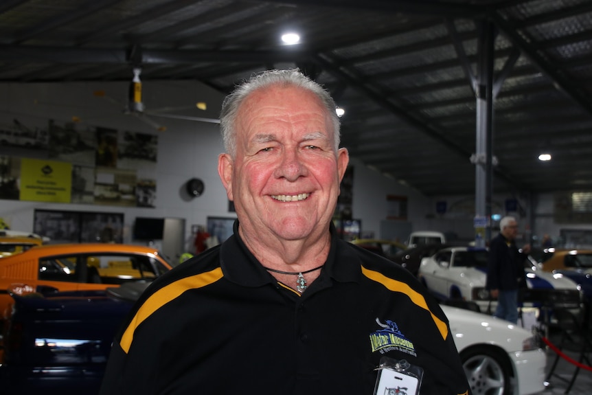 A man smiling in a polo shirt at a warehouse housing classic cars.