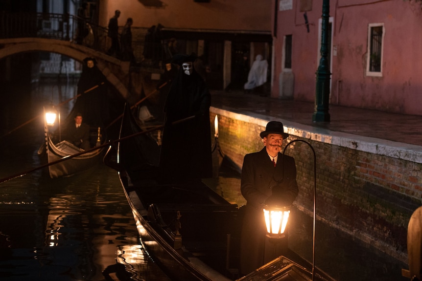 A film still showing a man standing in a gondola, lit by a street lantern