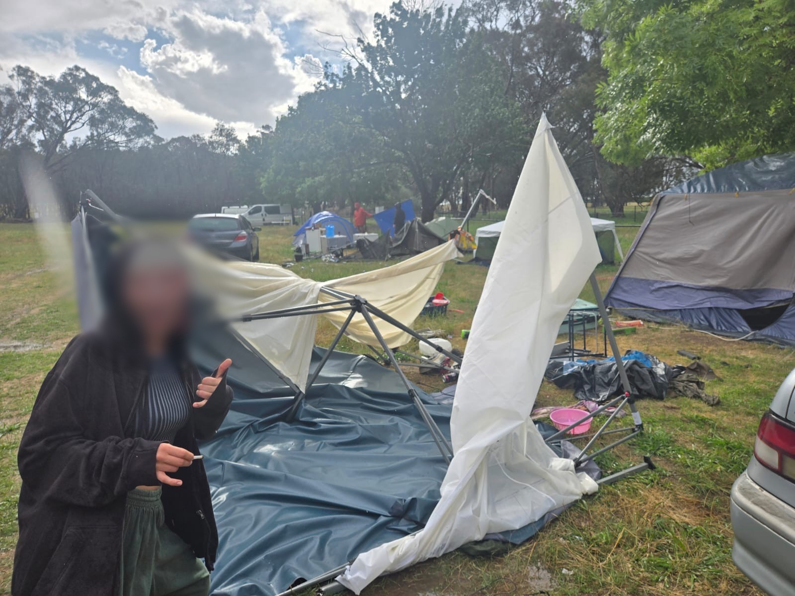 Uma mulher está em frente a uma tenda desabada.