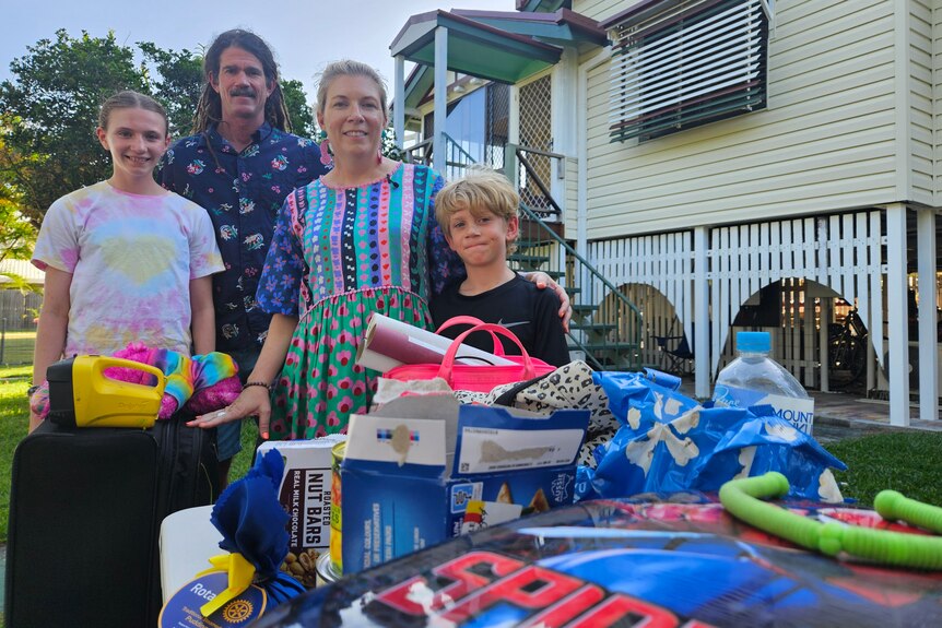 A family standing in their front yard, with a collection of household items on a table in frong of them.
