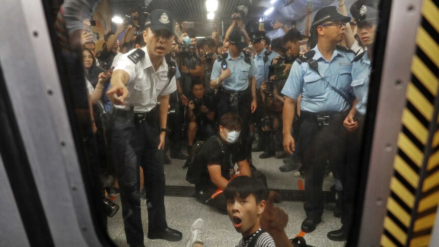 Two protesters surrounded by police officers while sitting on the floor at a Hong Kong train station
