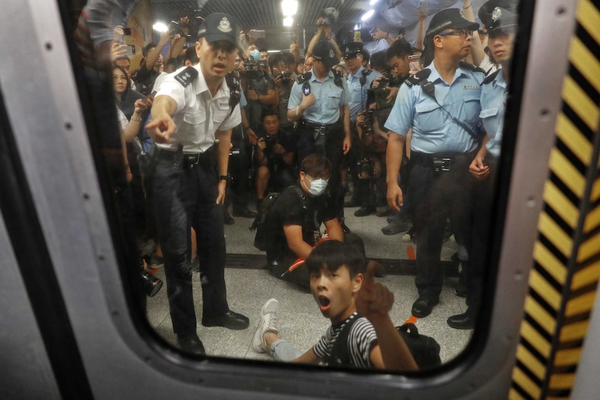 Two protesters surrounded by police officers while sitting on the floor at a Hong Kong train station