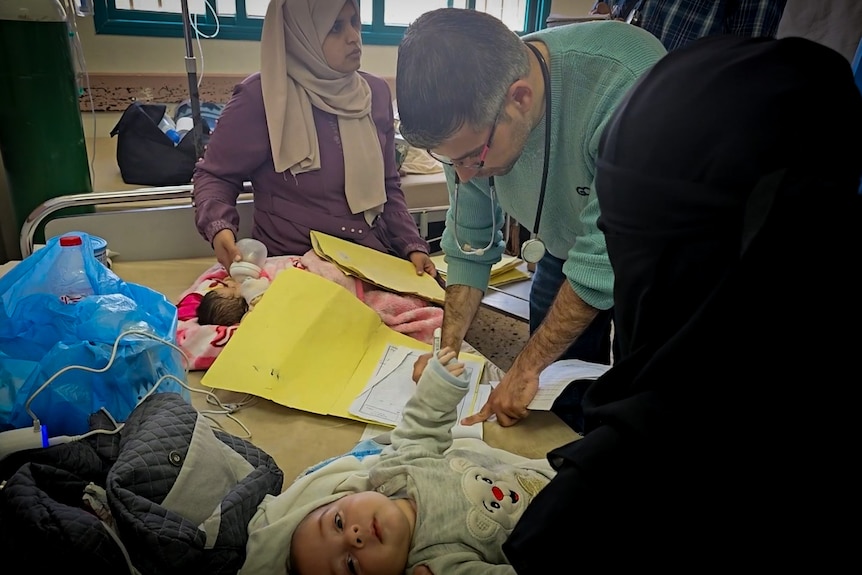 A doctor examines two babies on a hospital bed 