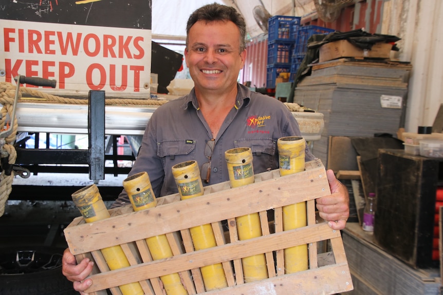 Miek Newman holding a rack of empty orange fireworks mortars 