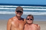 A naked man stands with his arm around a naked woman on a beach.