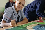 Matilda in her school uniform holding a paint brush, smiling.