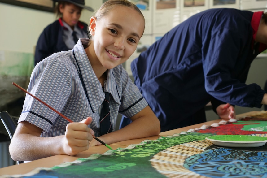 Matilda in her school uniform holding a paint brush, smiling.