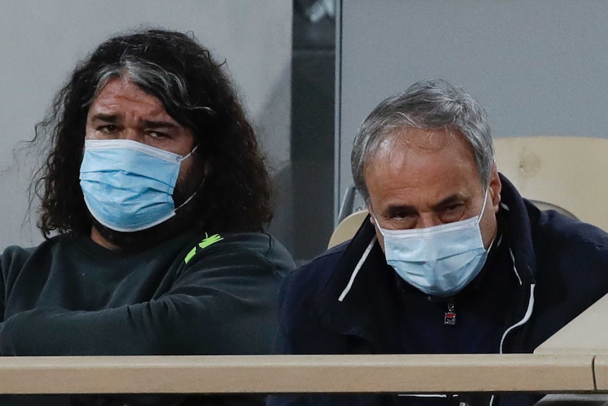 Two mask-wearing men sit next to each other in a box at the French Open tennis tournament.