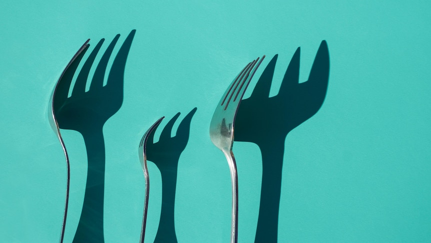 three forks and their shadows on a sea green background