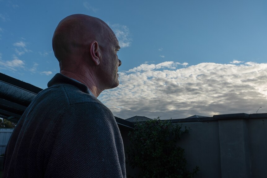 A man stands in a jumper looking up to a wide blue sky