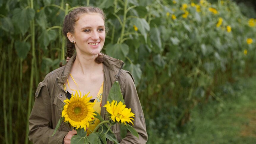 A young woman standing in a field holding a large sunflower to depict supporting women with autism spectrum disorder.