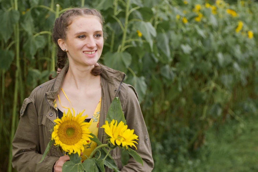 A young woman standing in a field holding a large sunflower to depict supporting women with autism spectrum disorder.