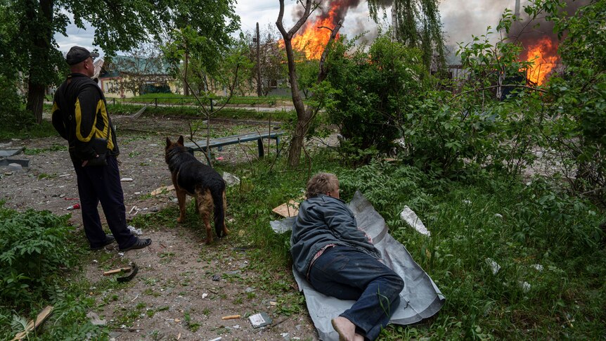A man lies on the ground as he watches his burning house destroyed by a Russian airstrike in Vovchansk.