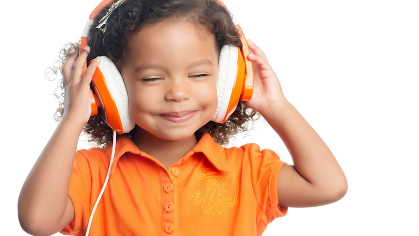Young child wearing big orange headphones and smiling. 