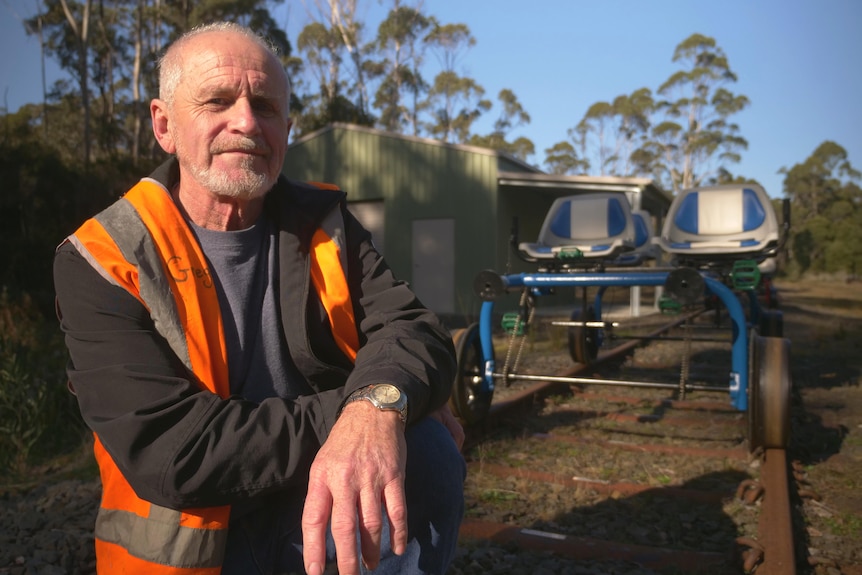 A man in a high vis vest crouched on a rail track, a rail bug in the background.