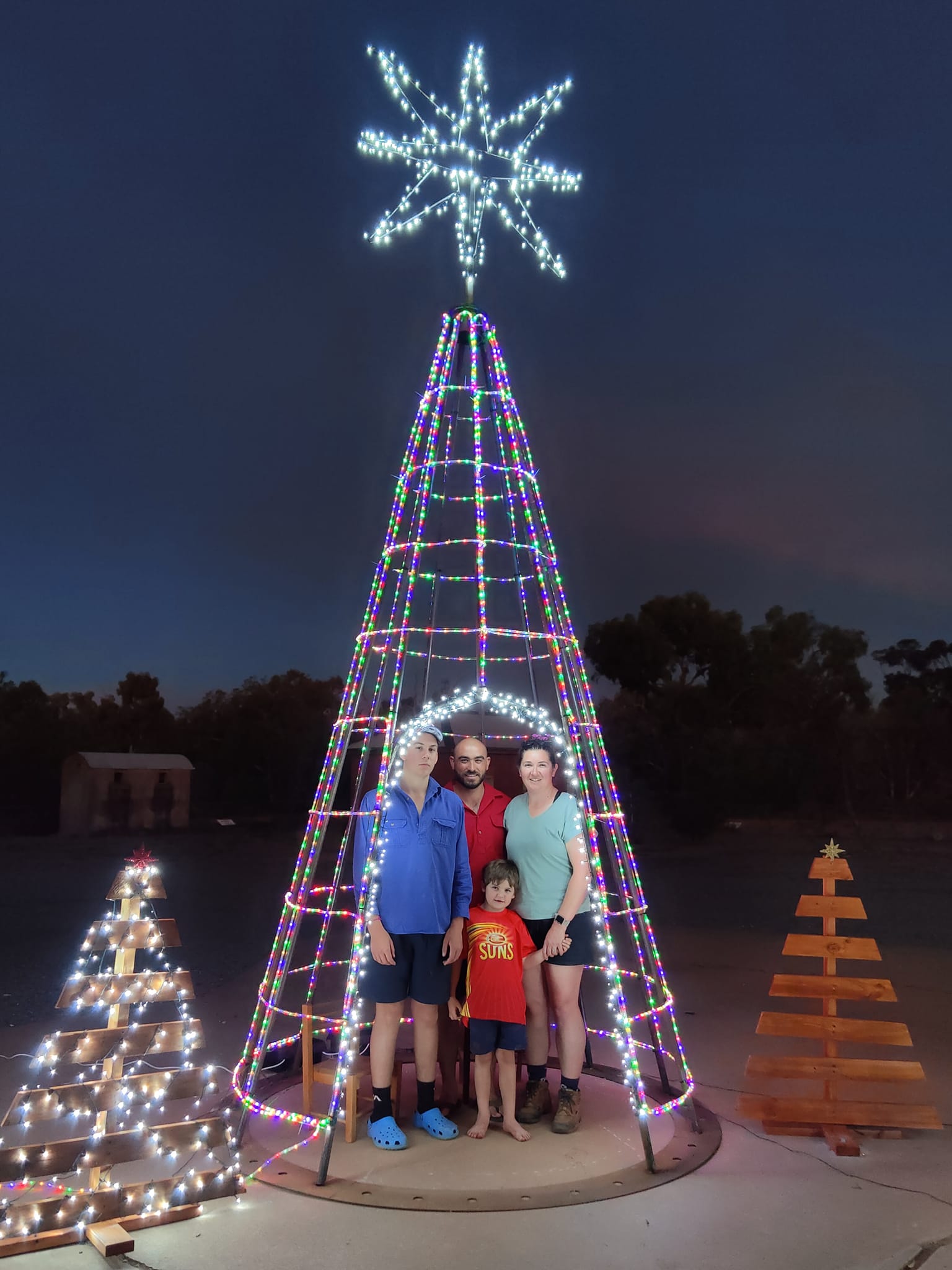 A family of four stand in the illuminated archway of a Christmas tree.