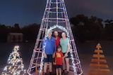 A family of four stand in the illuminated archway of a Christmas tree.
