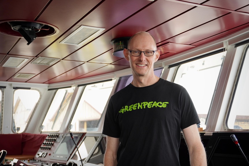 David Ritter stands inside the cabin of a ship wearing a Greenpeace T-shirt