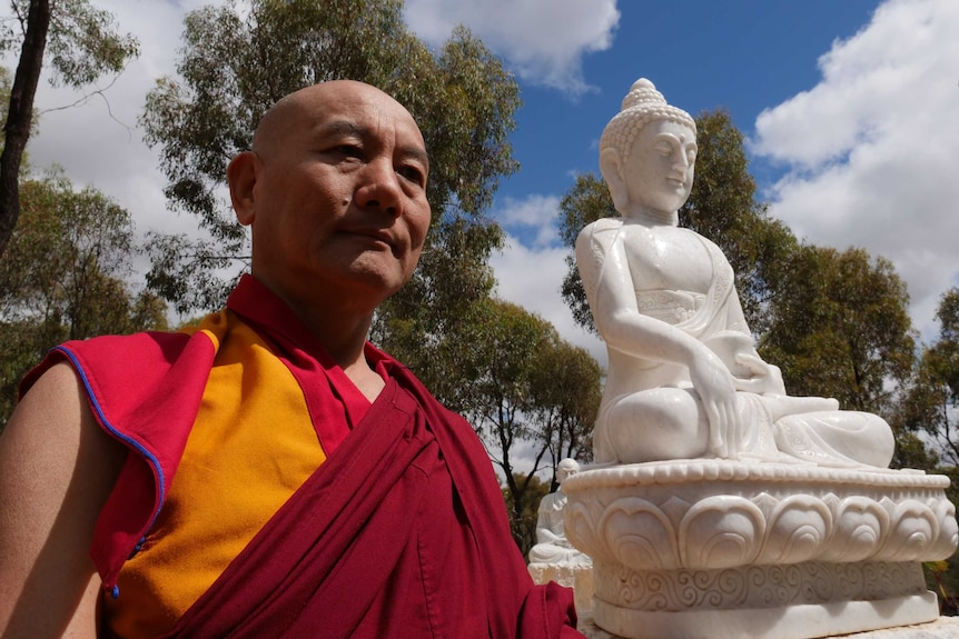 Geshe Rapten standing beside an aspect of the Buddha