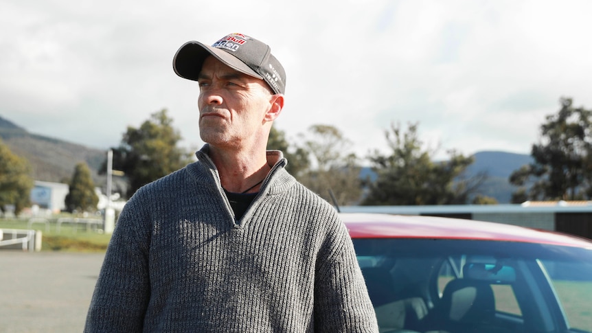 Jason Browne, wearing a cap, standing on the street in front of his car.