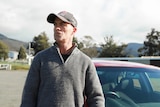 Jason Browne, wearing a cap, standing on the street in front of his car.