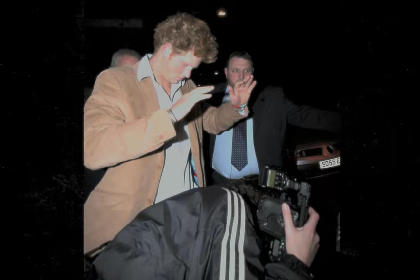 A paparazzi photographs Prince Harry at nighttime 