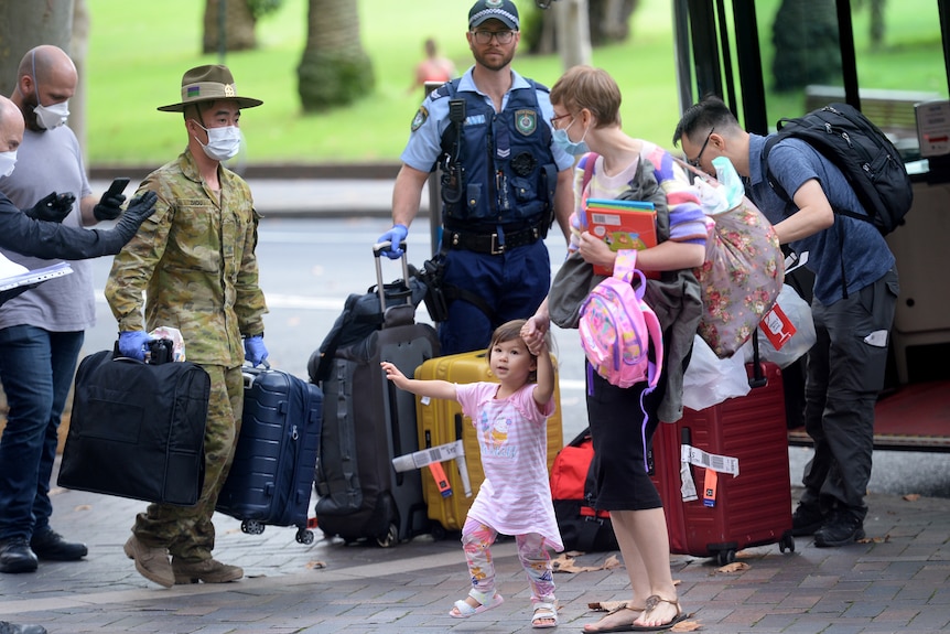 A young family disembark a bus with their luggage while a masked Australian soldier and policeman carry suitcases.